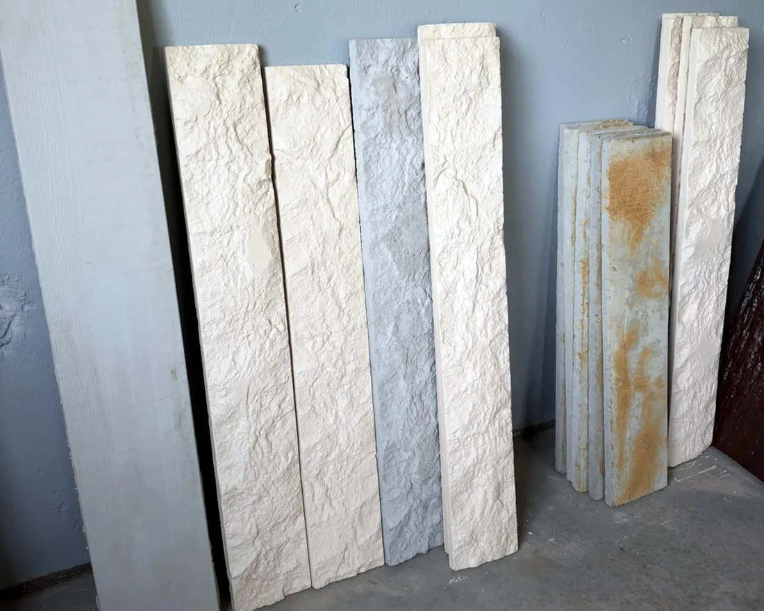Peças Art Cimento encostadas na parede: ripas com textura de madeira e pedras em relevo, em branco, cinza, marfim e ferrugem.